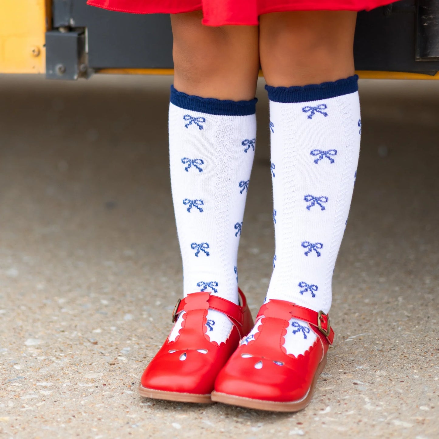 Child's legs wearing white socks with blue patterns and red shoes on a concrete floor.