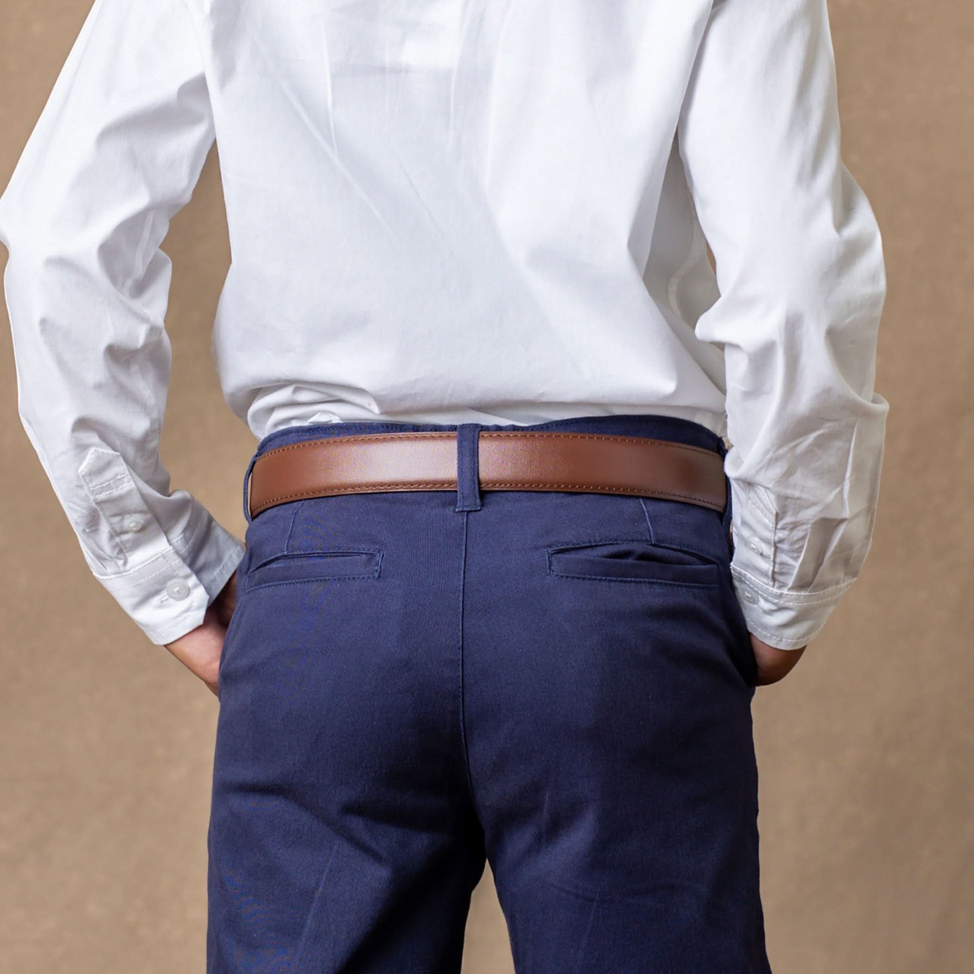 Person wearing a white shirt, navy pants, and a brown belt against a beige background