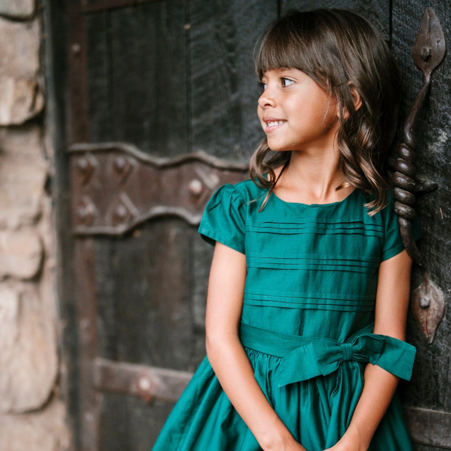 young girl outside wearing Hope & Henry organic pleated sateen party dress in deep green