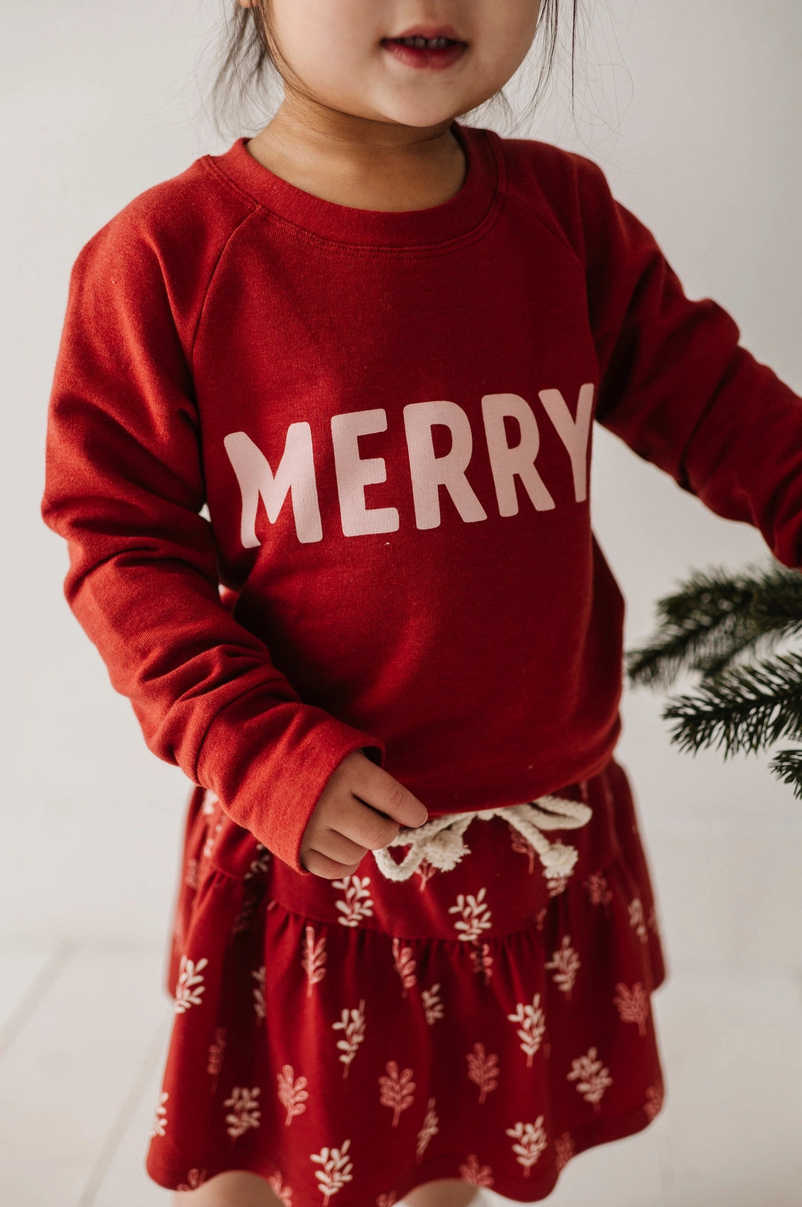 Child wearing a red 'MERRY' sweater with a white background