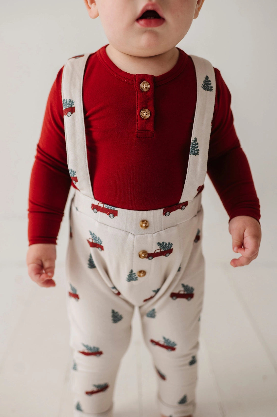 Child wearing a red shirt and white overalls with vehicle patterns on a plain background