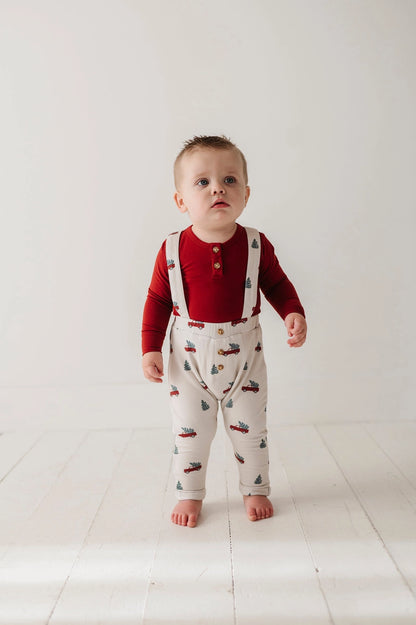 Baby wearing a red shirt and white overalls with vehicle pattern on a light background