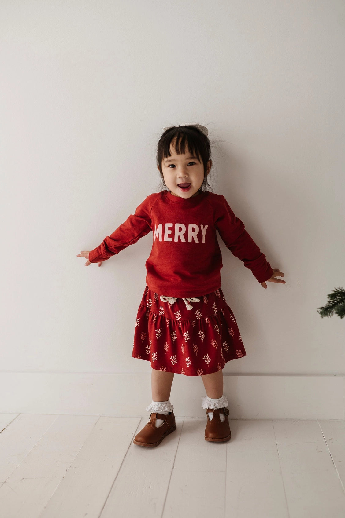 Child wearing a red 'MERRY' sweater and red skirt with white patterns on a white background