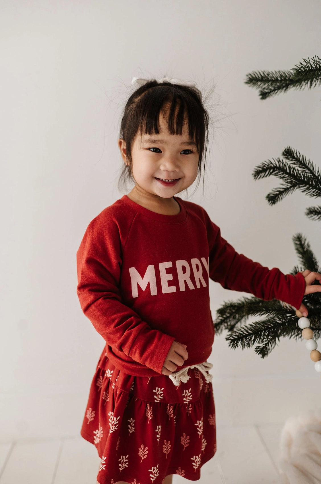 Child wearing a red 'Merry' sweater with a white background