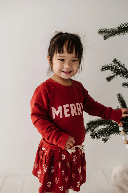Child wearing a red 'Merry' sweater with a white background