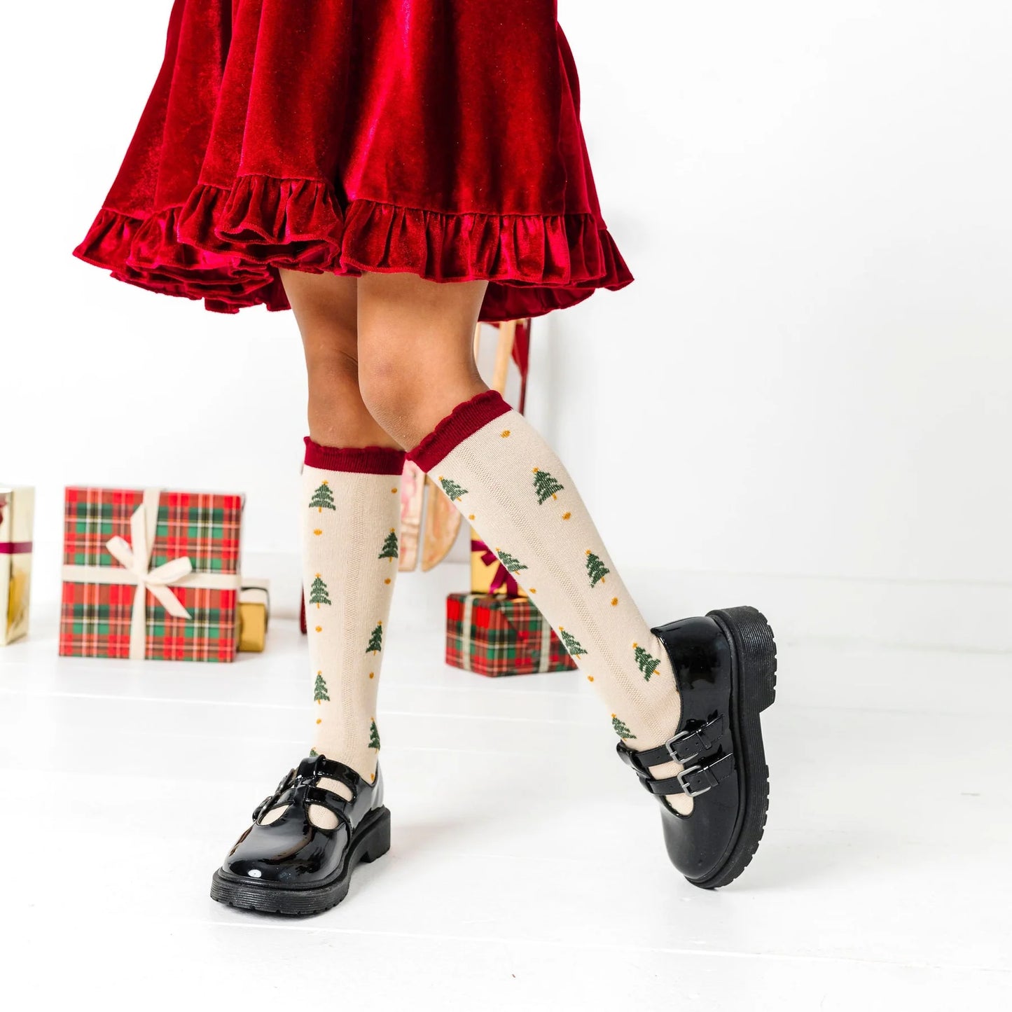 Person wearing a red skirt and black shoes with Christmas-themed socks on a white background.