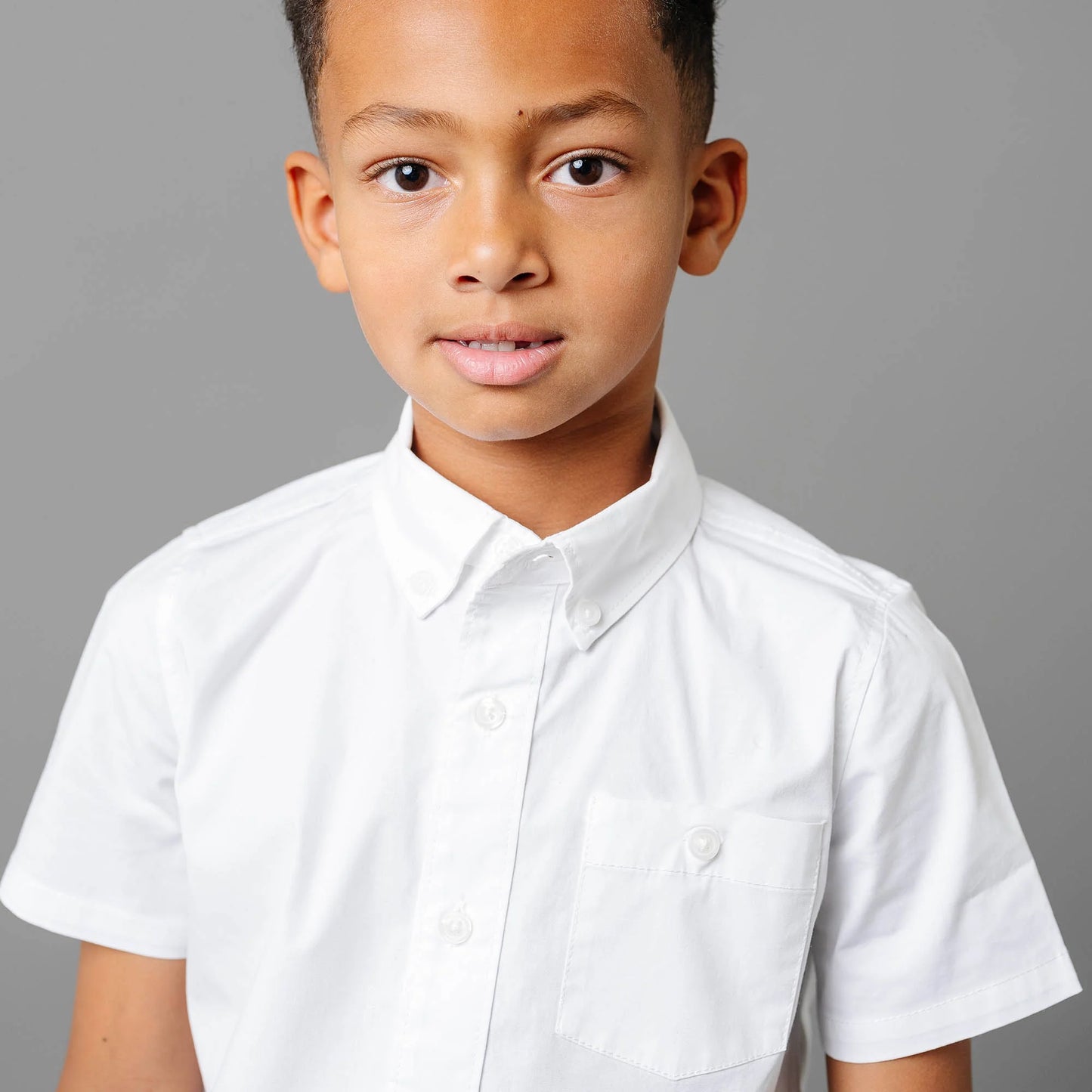 closeup of model boy wearing Boys white short sleeve organic cotton stretch poplin button-down shirt by Hope and Henry.