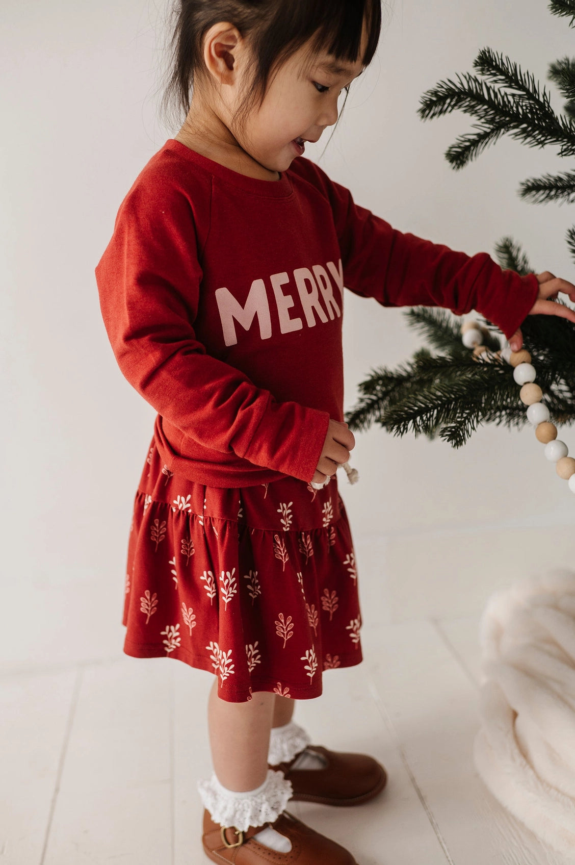 Child wearing a red 'Merry' sweater with a white background
