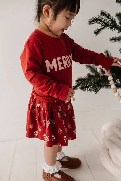 Child wearing a red 'Merry' sweater with a white background