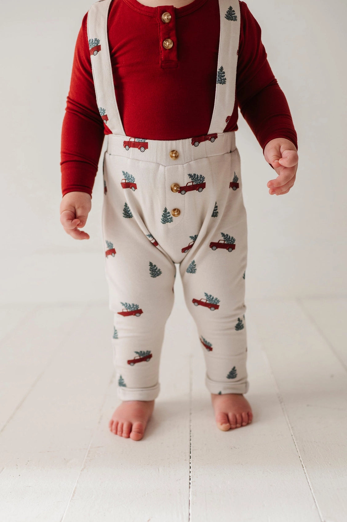 Child wearing a red shirt and patterned pants with suspenders on a white background