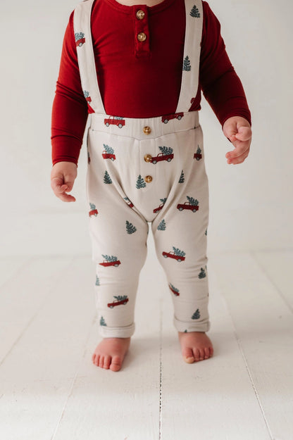 Child wearing a red shirt and patterned pants with suspenders on a white background